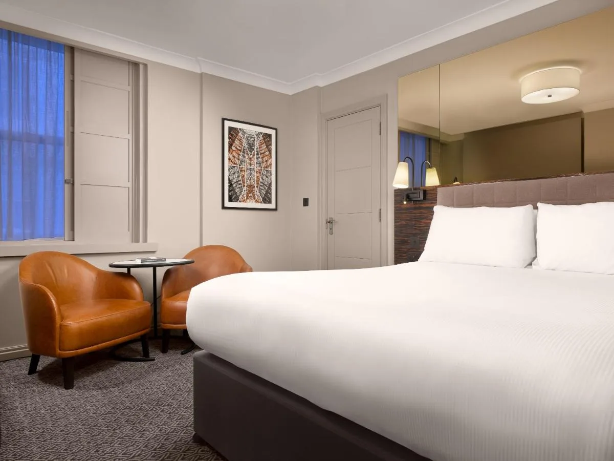 a hotel room with a large bed and a chair at Strand Palace in London
